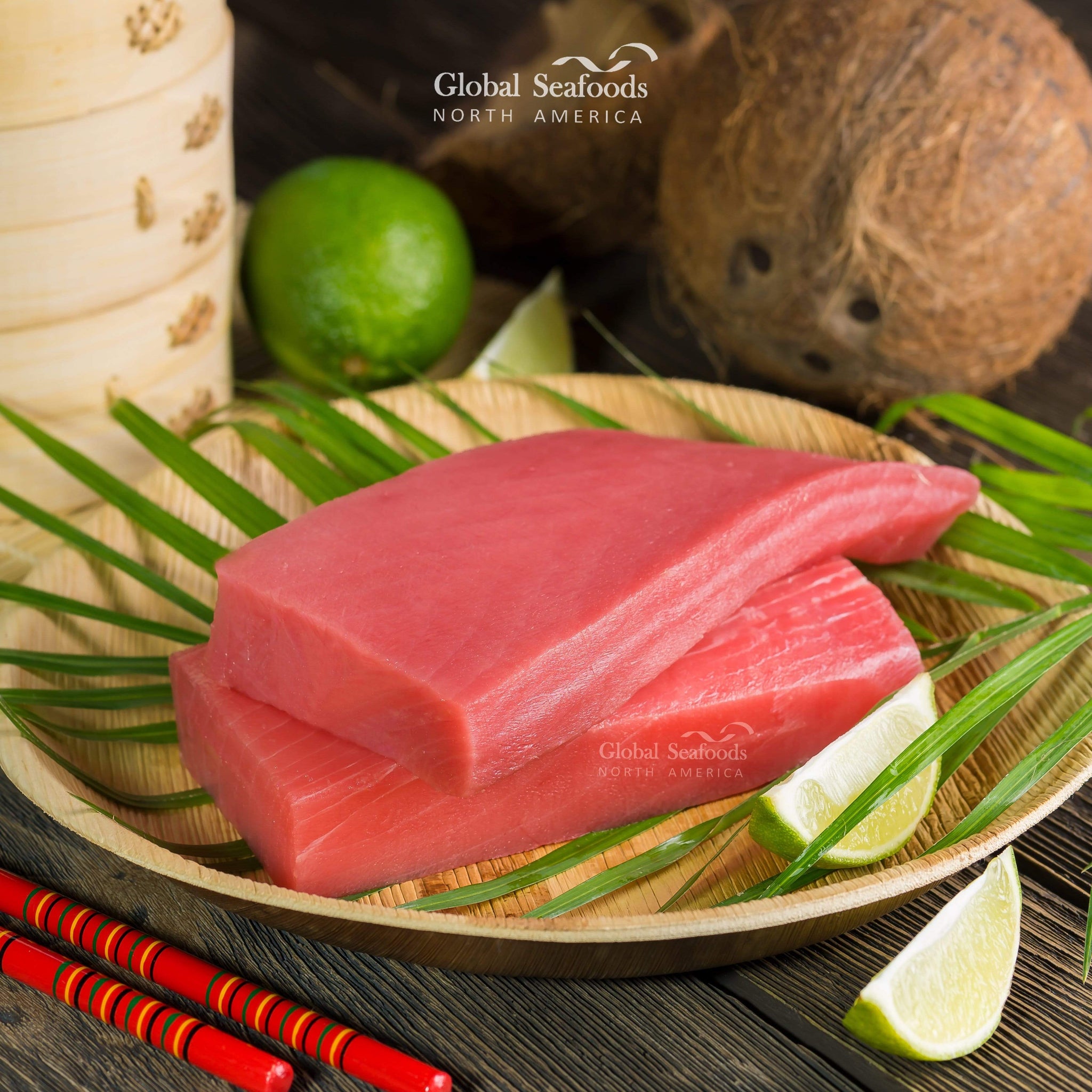 Two Saku tuna blocks placed on a wooden plate, with lime slices and a cracked coconut in the background for a fresh and tropical presentation