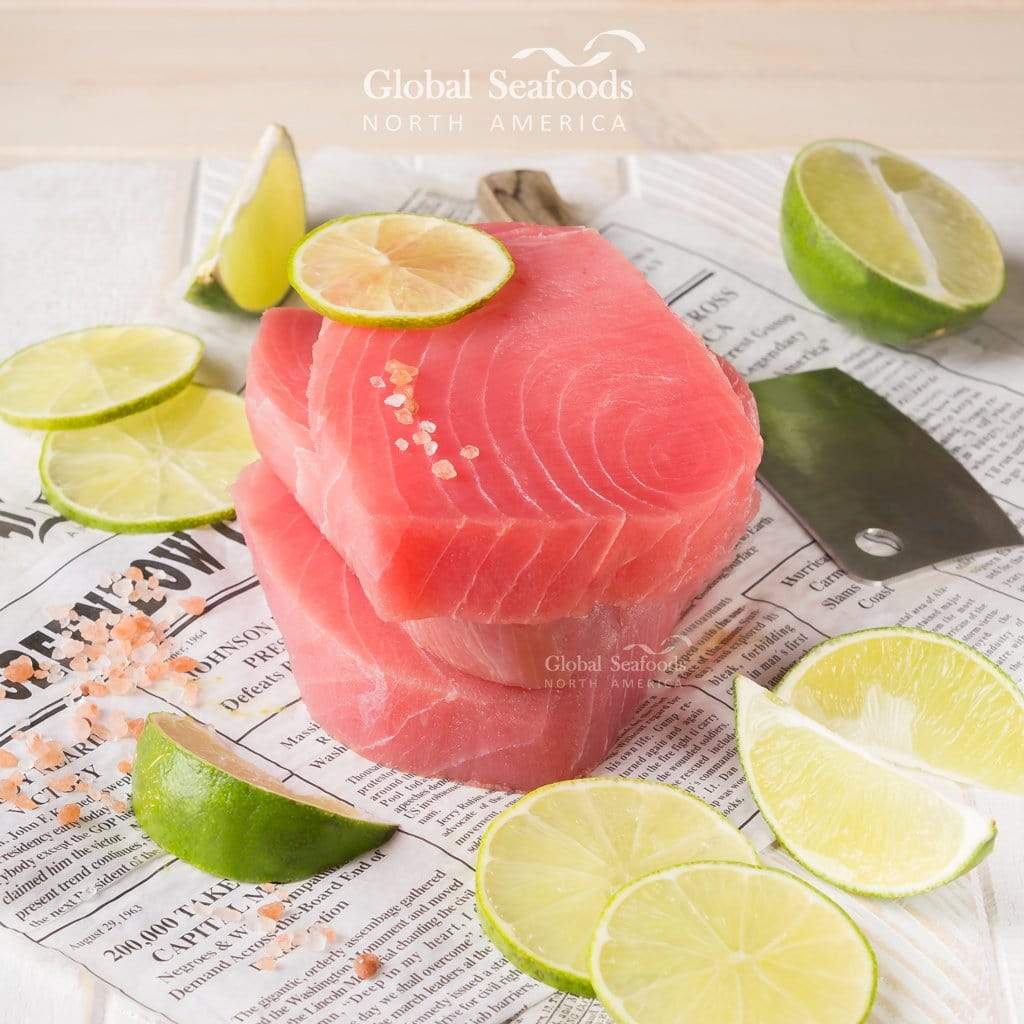 Three ahi tuna steaks placed on newspaper, surrounded by sliced limes for a fresh, market-style seafood presentation