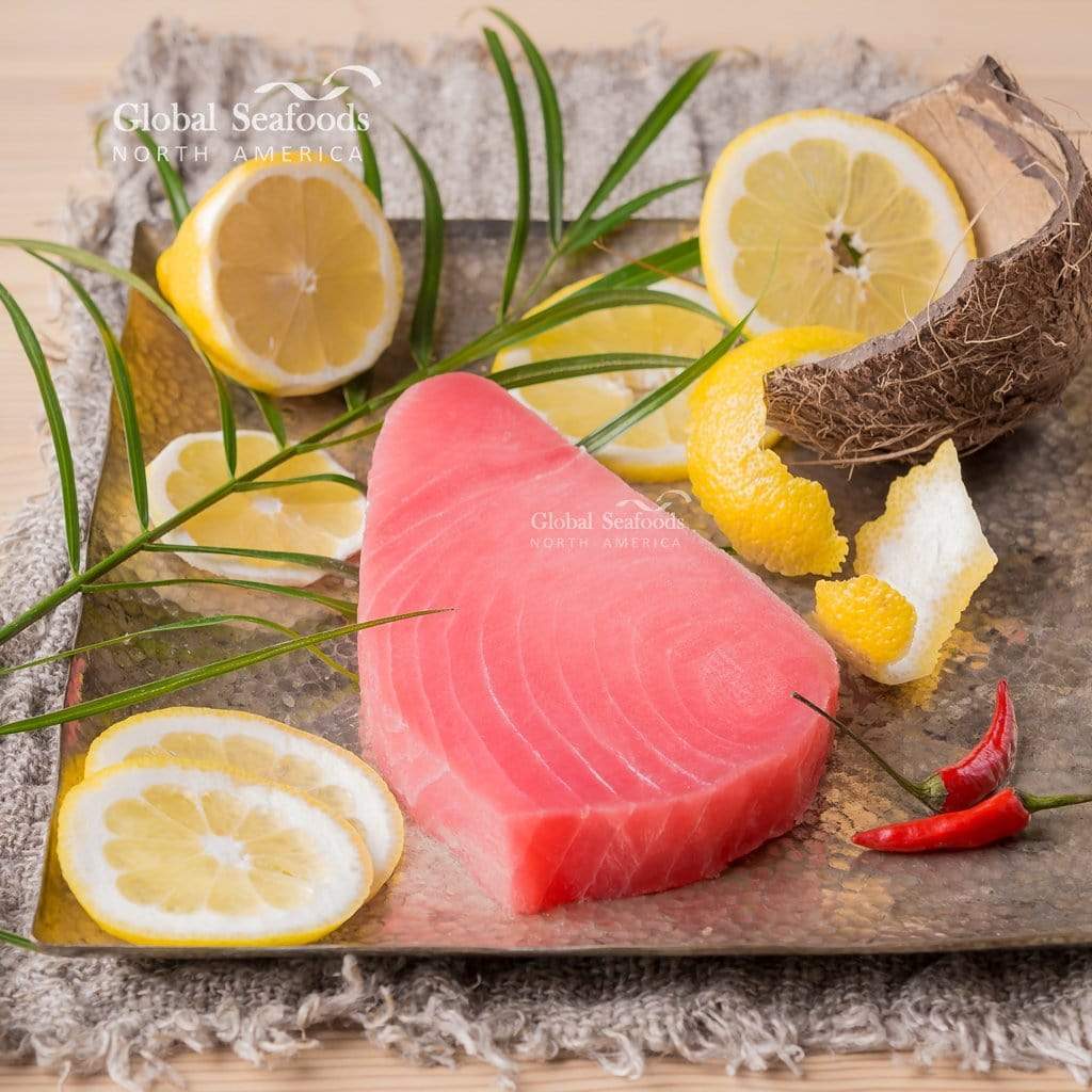 One Ahi tuna steak served on a square silver platter with lemon slices and a cracked coconut, creating a vibrant and tropical seafood presentations