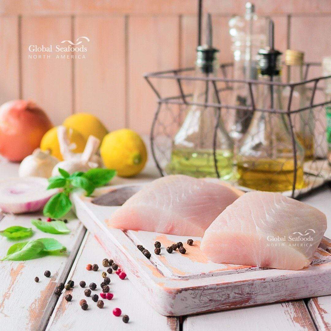 Mahi Mahi fillet portions arranged on a wooden board, with two bottles of oil and fresh lemons in the background, styled for a fresh and vibrant seafood preparation